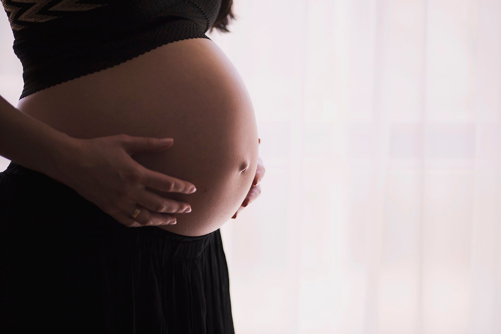 Une femme enceinte pose les mains sur son ventre, dans une lumière douce.
