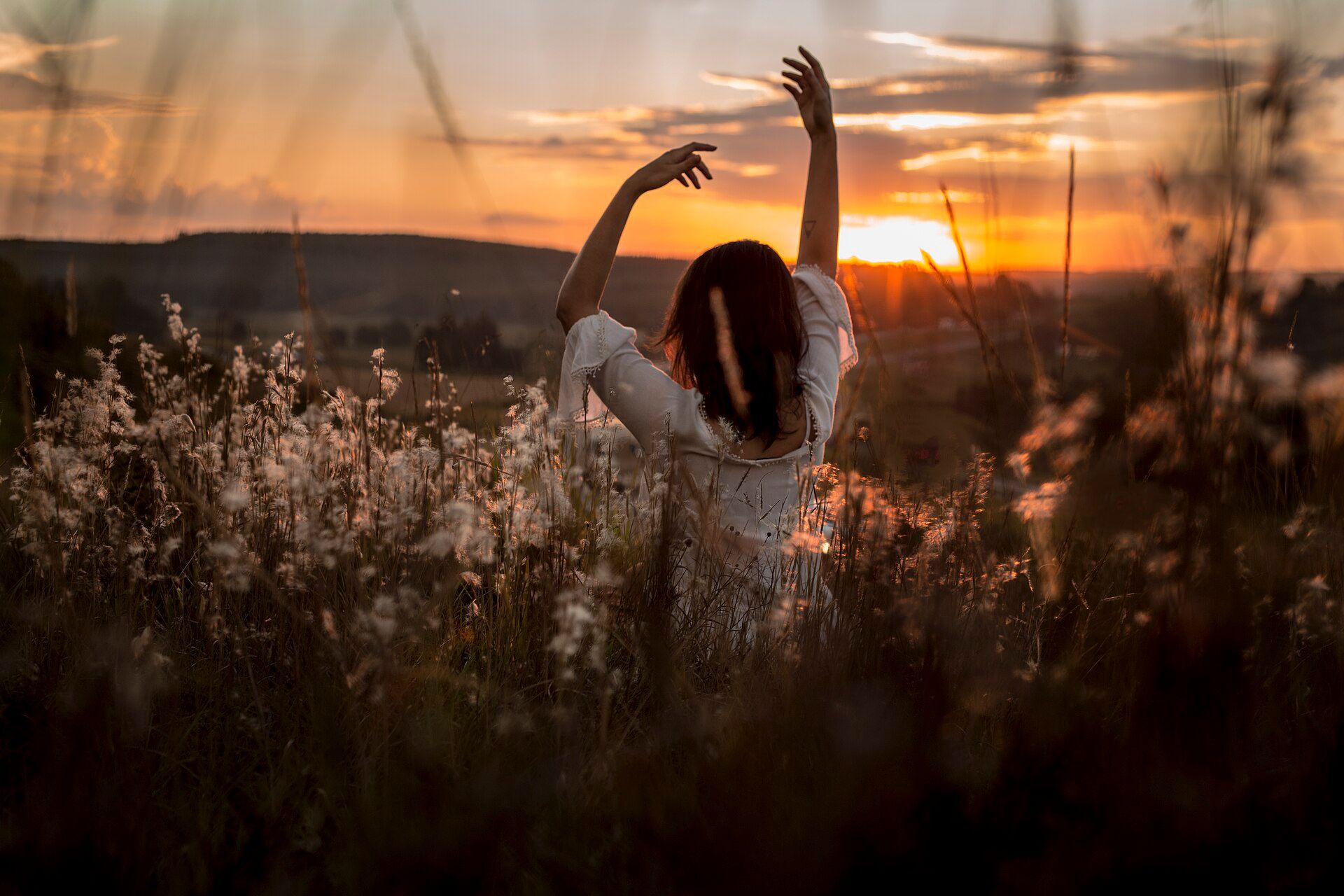 Une femme étire les bras vers le ciel au lever du soleil, dans un champ.
