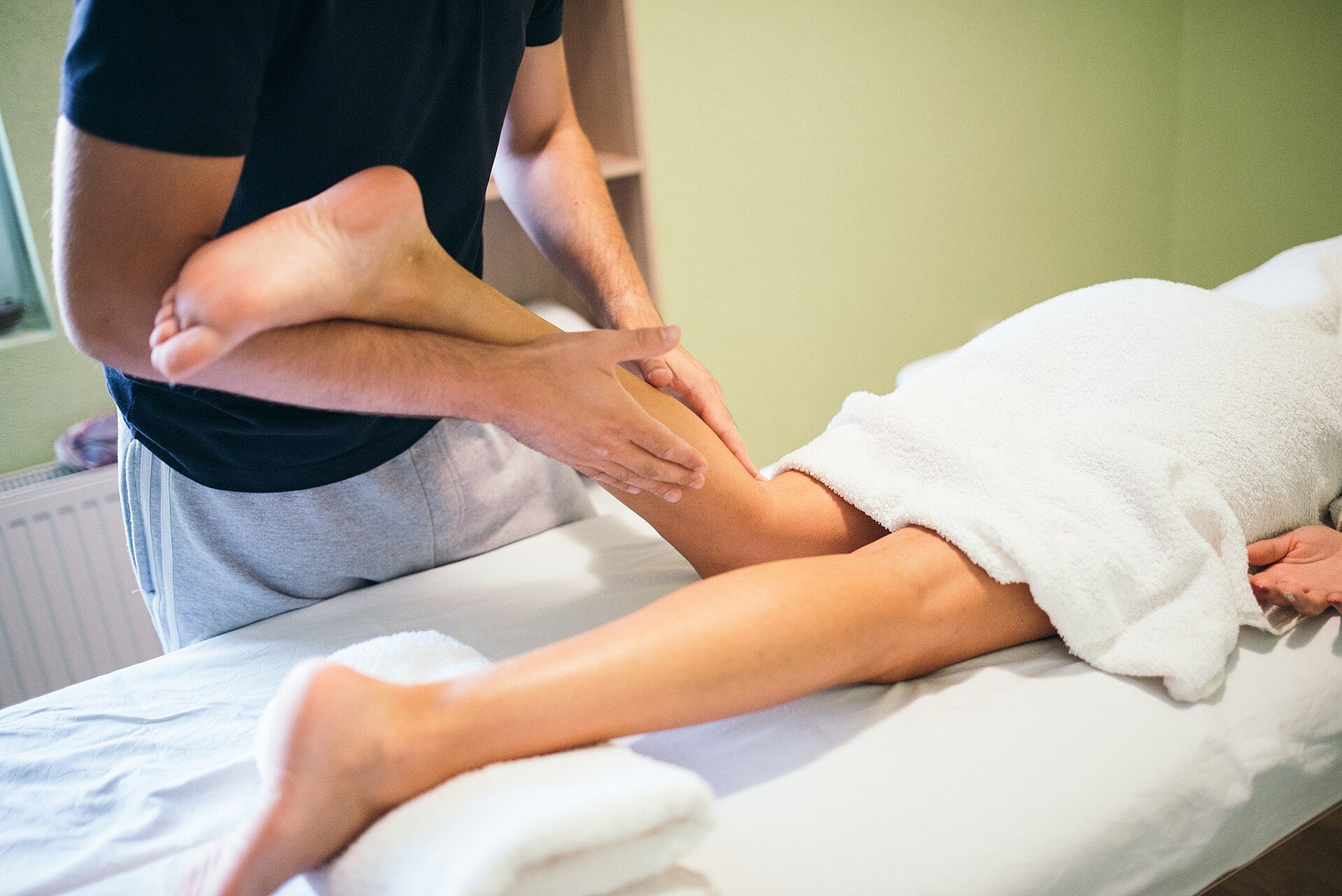 Une séance de thérapie manuelle sur la jambe d'une patiente allongée sur une table de soin.